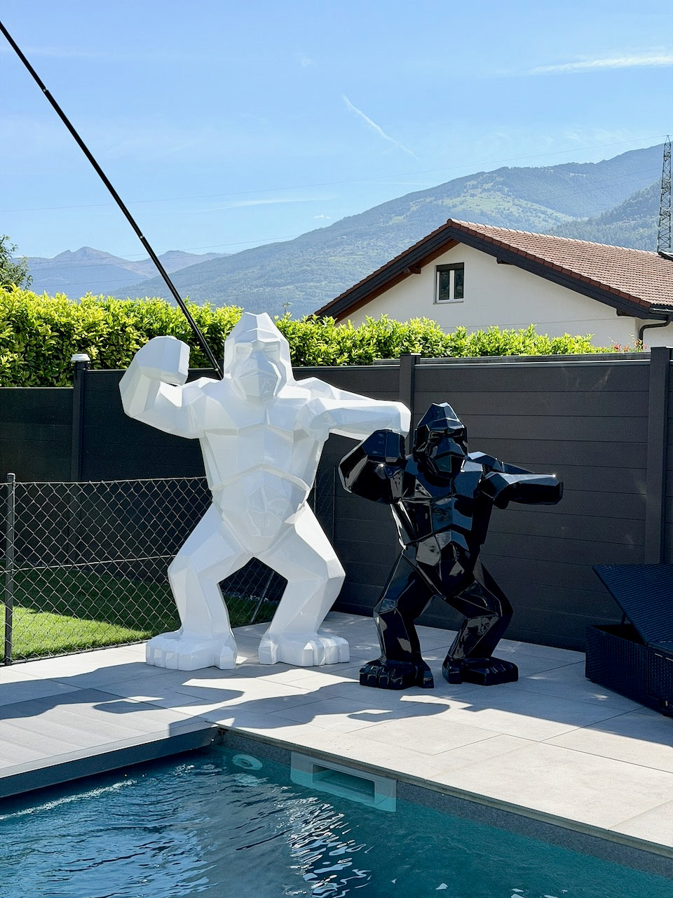 Kongari Collection — sculpture gorille origami monumentale H200 cm Blanc Alpin face au format H150 cm Noir Onyx, au bord d'une piscine en Valais
