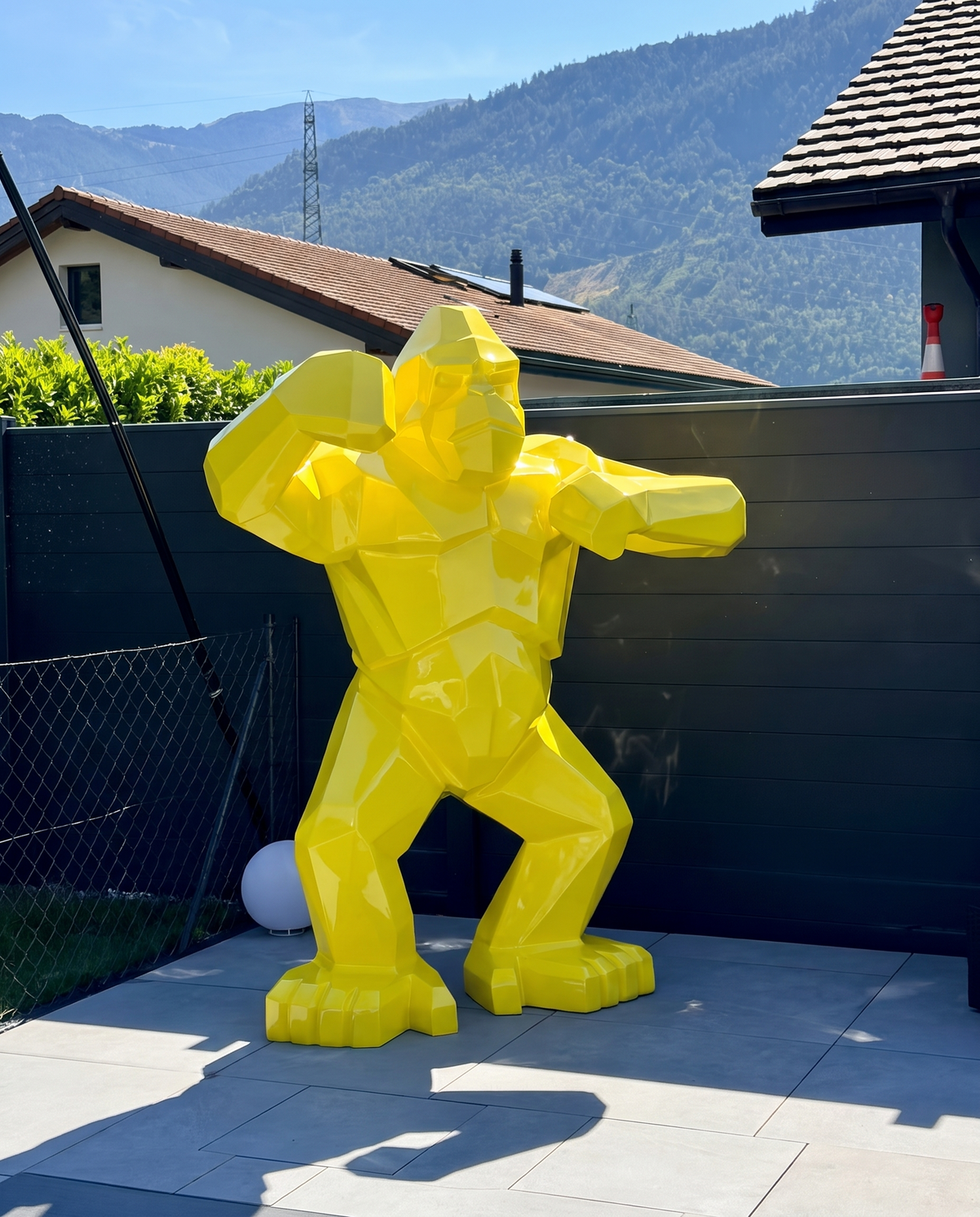 Kongari Collection — sculpture gorille origami Jaune Helios H200 cm pour intérieur et extérieur, résine laquée anti-UV, installée dans un jardin face aux Alpes suisses