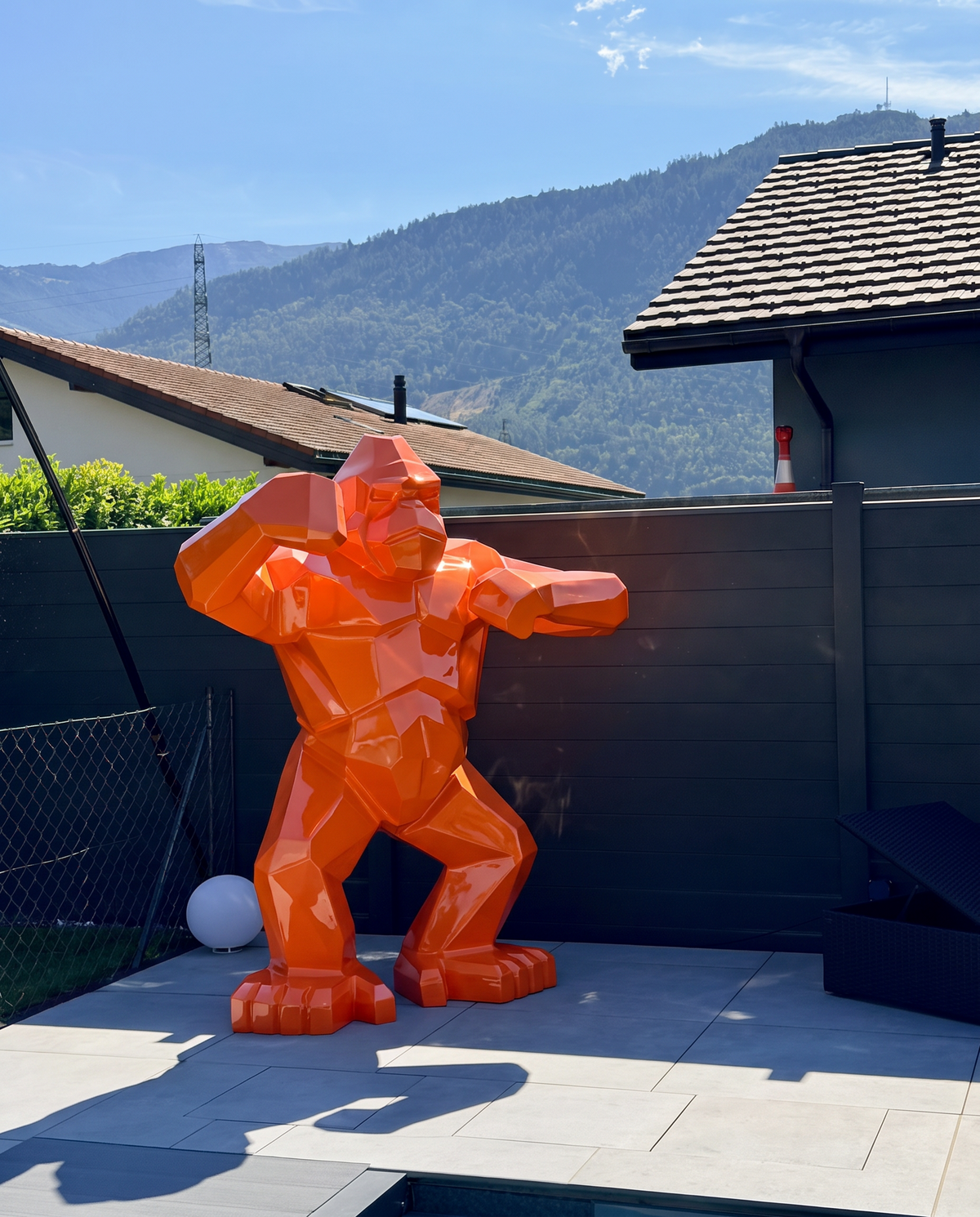 Kongari Collection — sculpture gorille origami Orange Fusion H200 cm pour intérieur et extérieur, résine laquée anti-UV, installée dans un jardin face aux Alpes suisses
