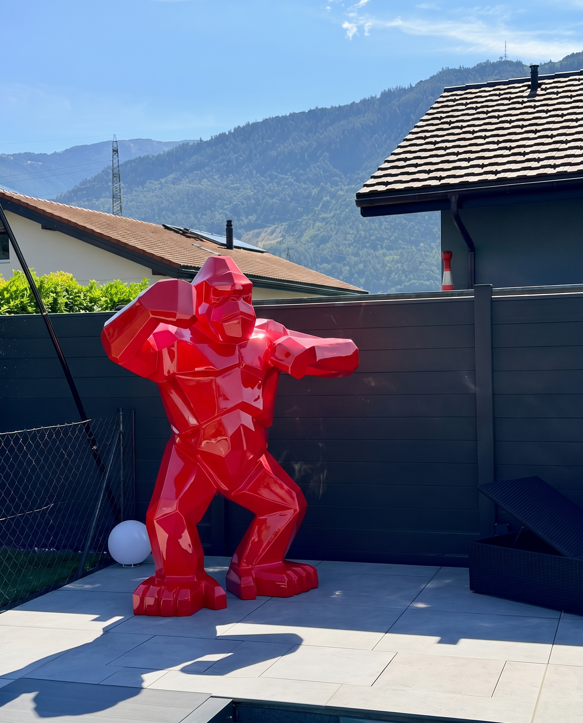 Kongari Collection — sculpture gorille origami Rouge Helvete H200 cm pour intérieur et extérieur, résine laquée anti-UV, installée dans un jardin face aux Alpes suisses
